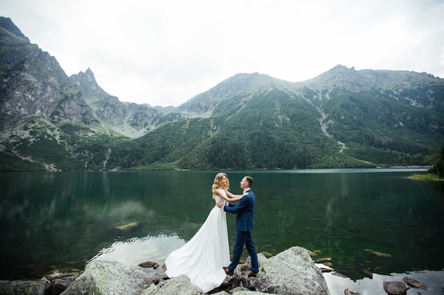 Coppia sposata (sposa e sposo) sposarsi in montagna. abbracciarsi nel mezzo di un lago con una montagna