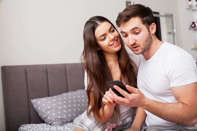 Coppia sul letto guardando smartphone e sorridente