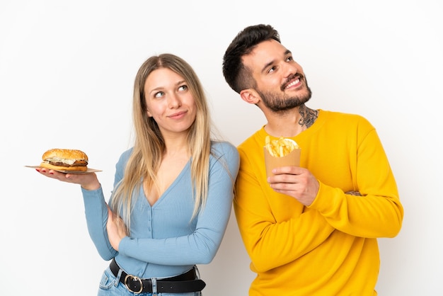 Coppia tenendo hamburger e patatine fritte su sfondo bianco isolato guardando in alto mentre sorride