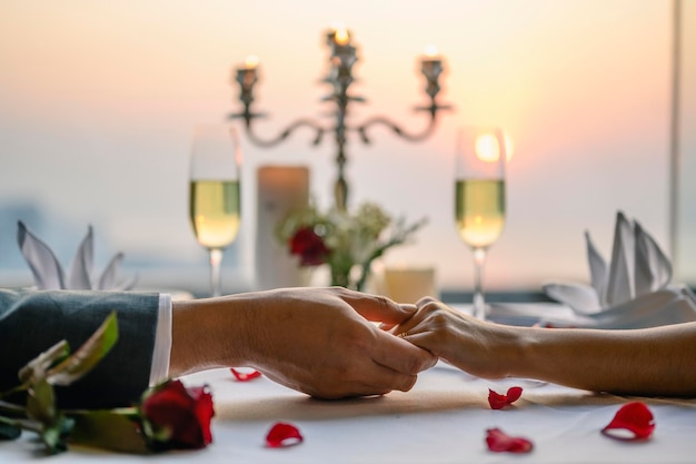 Coppia tenendosi per mano con una cena al ristorante in vista del tramonto. San Valentino, coppia, luna di miele, cena, vino, concetto romantico.