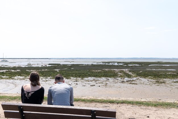 Coppia uomo e donna seduta sulla spiaggia e guardare il mare calmo della bassa marea