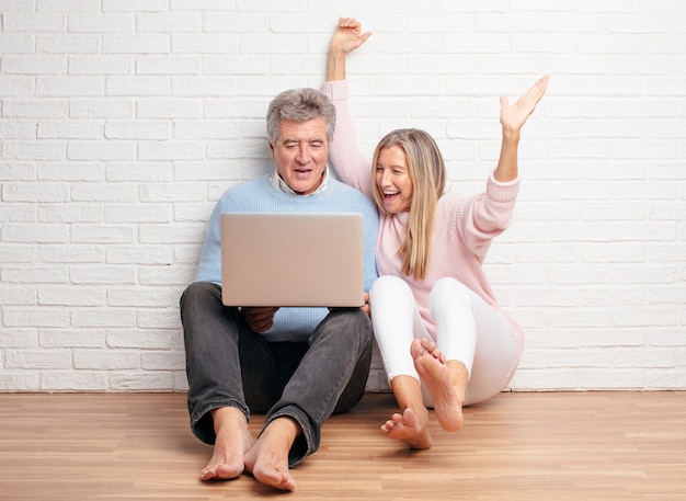 Coppie abbastanza senior che si siedono sul loro pavimento della casa con un computer portatile