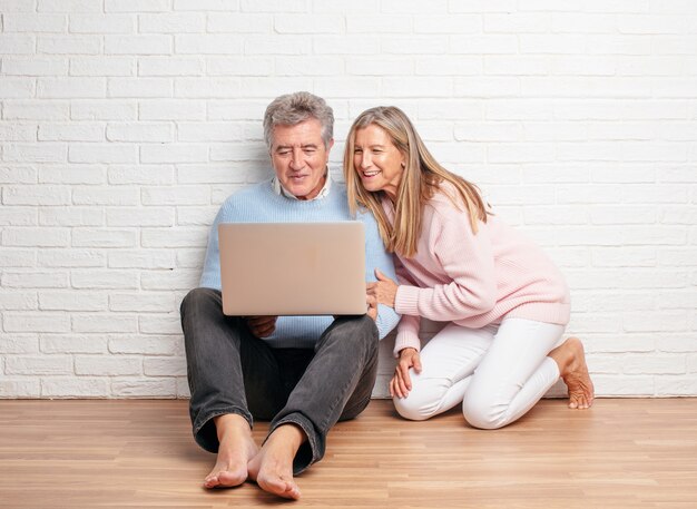 Coppie abbastanza senior che si siedono sul loro pavimento della casa con un computer portatile