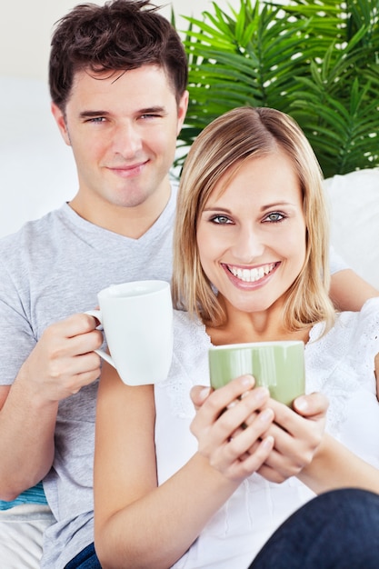 Coppie adorabili che riposano sul sofà che tiene le tazze di caffè