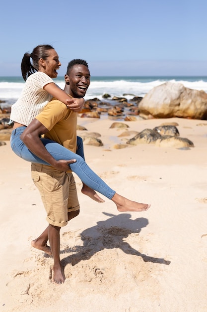 Coppie afroamericane che trasportano sulle spalle su una spiaggia in riva al mare. stile di vita sano, tempo libero nella natura.