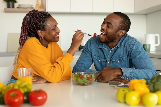 Coppie afroamericane romantiche che mangiano insalata sana in cucina moglie felice che alimenta suo marito