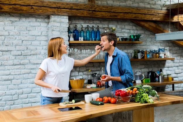 Coppie allegre adorabili che cucinano insieme cena e che si divertono alla cucina rustica