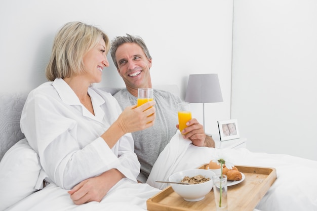 Coppie allegre che mangiano succo d&#39;arancia a colazione a letto