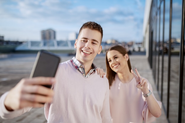 Coppie allegre sveglie che stanno all'aperto e che prendono selfie