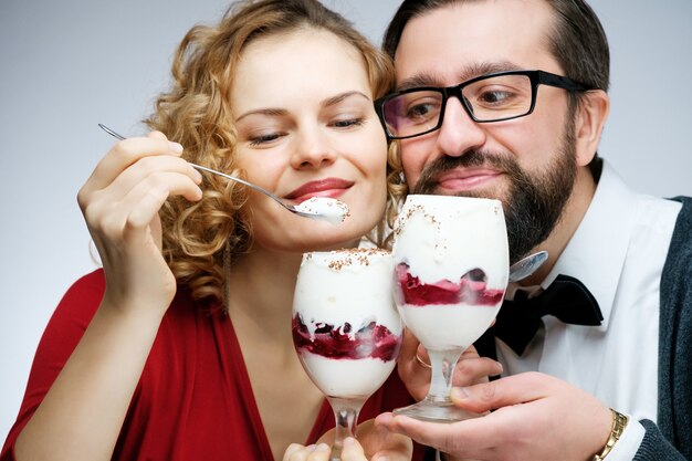 Coppie amorose che mangiano insieme il gelato alla ciliegia. L'uomo con la ragazza con il farfallino in un vestito rosso su sfondo bianco