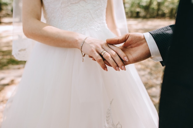 Coppie amorose che si tengono per mano con gli anelli contro il vestito da sposa