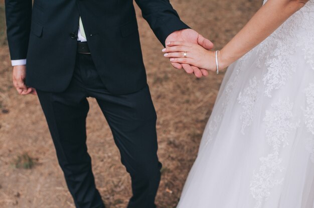 Coppie amorose che si tengono per mano con gli anelli contro il vestito da sposa