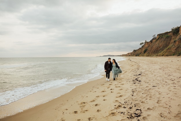 Coppie amorose di nozze che camminano sulla spiaggia. Bella coppia di sposi sul loro servizio fotografico di matrimonio in riva al mare