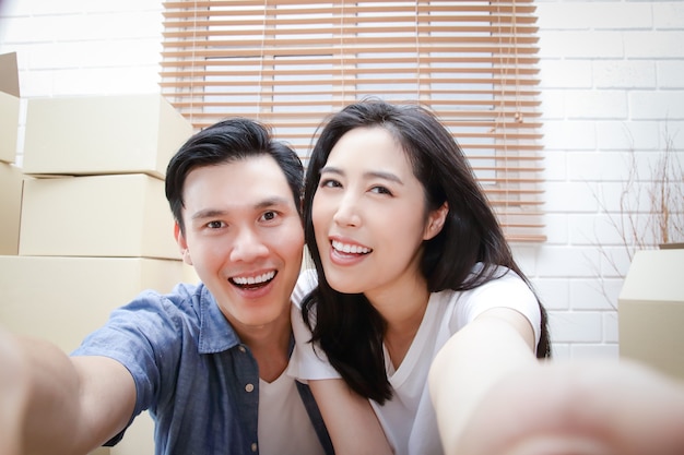 Coppie asiatiche felici che entrano nella nuova casa Prendete uno smartphone e fate un selfie.