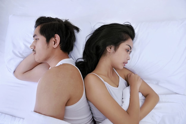Coppie asiatiche turbate che hanno problemi con la menzogne parallelamente nel letto che affronta nelle direzioni opposte