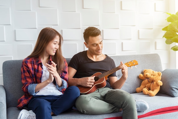 Coppie che giocano ukulele al divano. Vita felice in vacanza