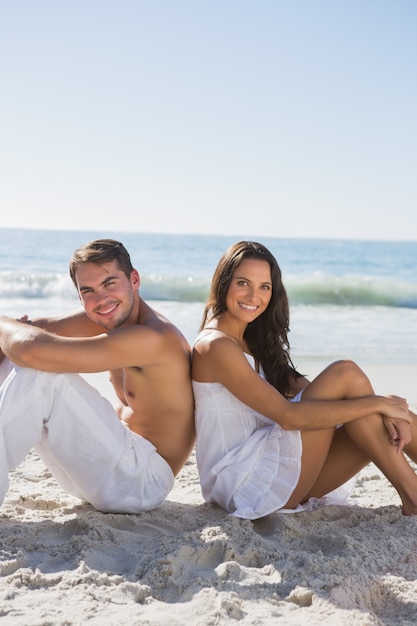 Coppie che si siedono di nuovo alla sabbia sulla schiena che sorride alla macchina fotografica