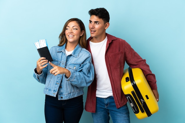 Coppie del viaggiatore che tengono una valigia sull'azzurro che presenta un'idea mentre guardando sorridente verso