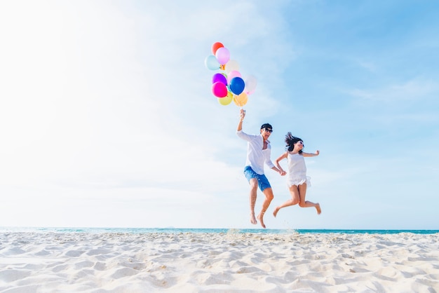 Coppie dell&#39;amante di felicità che tengono i palloni variopinti e che saltano sulla spiaggia nel giorno soleggiato