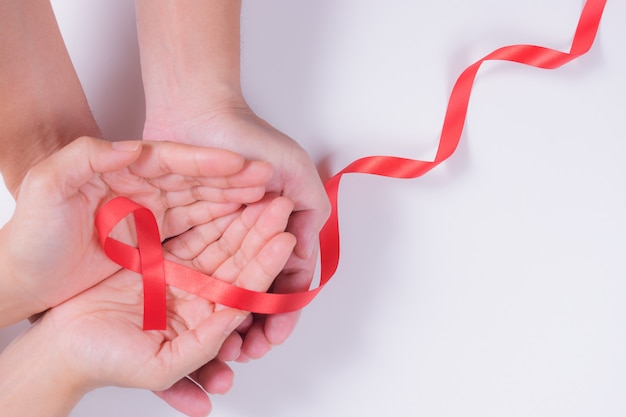 Coppie delle mani che tengono nastro rosso, concetto di consapevolezza del hiv, giornata mondiale contro l'AIDS.