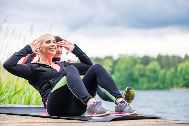 Coppie di sport che fanno addominali all&#39;aperto al fiume