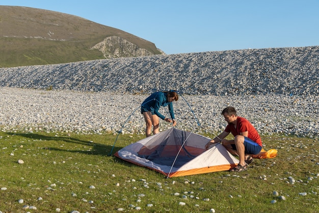 Coppie di stile di vita all'aperto della gente di campeggio che montano una tenda in spiaggia rocciosa della natura.