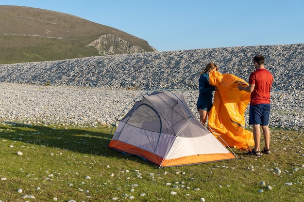 Coppie di stile di vita all'aperto della gente di campeggio che montano una tenda in spiaggia rocciosa della natura.