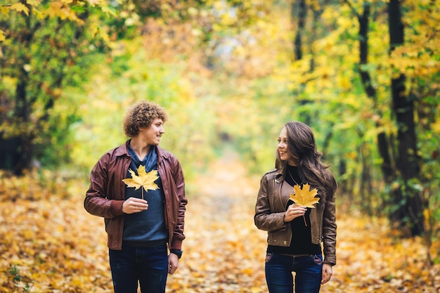 Coppie felici amorose in autunno nel parco che tiene le foglie di acero di autunno nelle mani