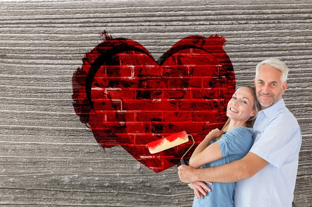 Coppie felici che abbracciano e che tengono il rullo di vernice contro il muro di mattoni rosso