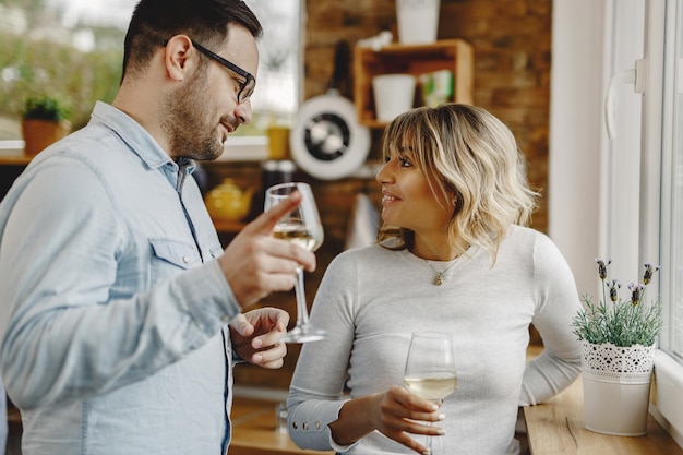 Coppie felici che comunicano bevendo vino vicino alla finestra in cucina