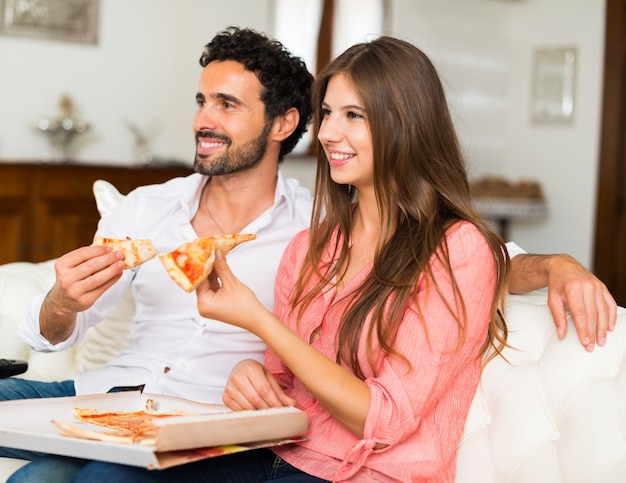 Coppie felici che guardano televisione mentre mangiando pizza.