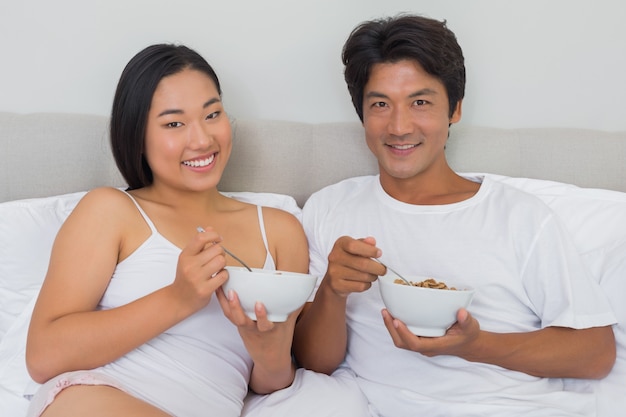 Coppie felici che mangiano prima colazione a letto a casa nella camera da letto