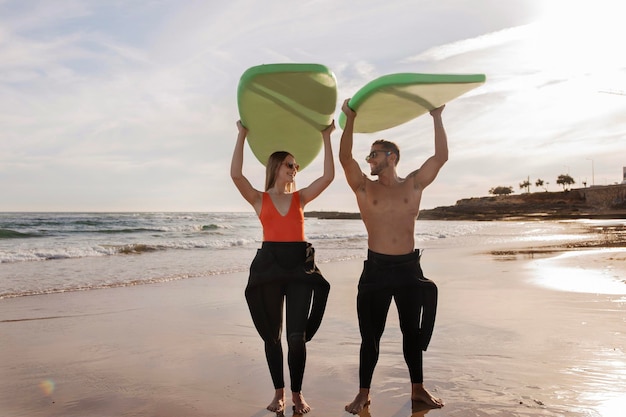 Coppie felici che si divertono sulla spiaggia tenendo le tavole da surf sopra le loro teste