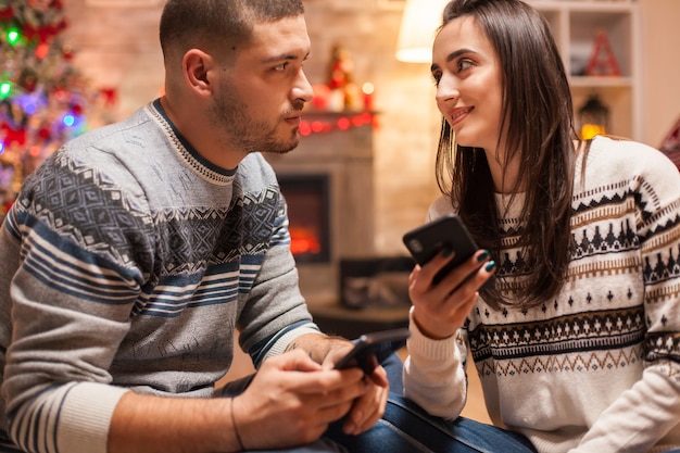 Coppie felici che si guardano negli occhi a natale. Navigazione sul telefono.