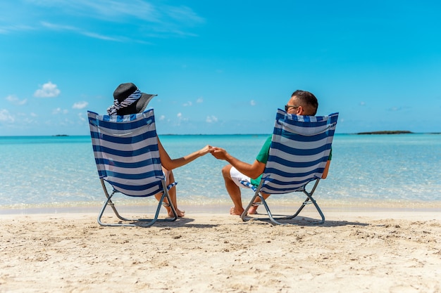 Coppie felici che si siedono in sedie su una spiaggia tropicale