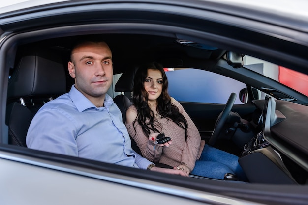 Coppie felici che si siedono nella nuova automobile e che sorridono nel salone