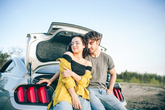 Coppie felici del viaggiatore che si siedono nel bagagliaio aperto dell'auto e guardare l'alba.