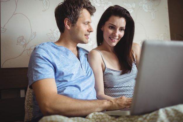 Coppie felici facendo uso del computer portatile sul letto