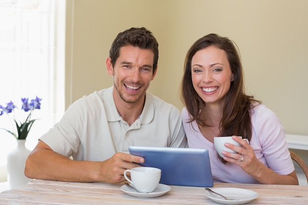 Coppie felici facendo uso della compressa digitale mentre mangiando caffè