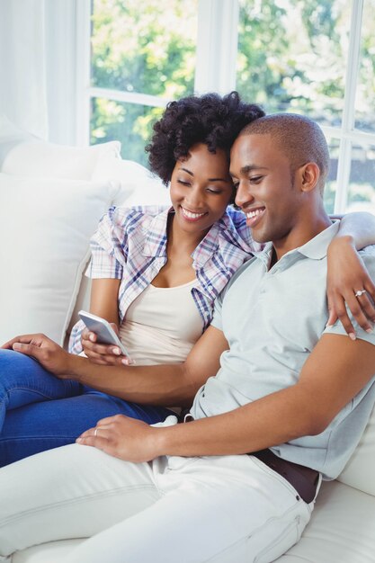 Coppie felici facendo uso dello smartphone sul sofà nel salone