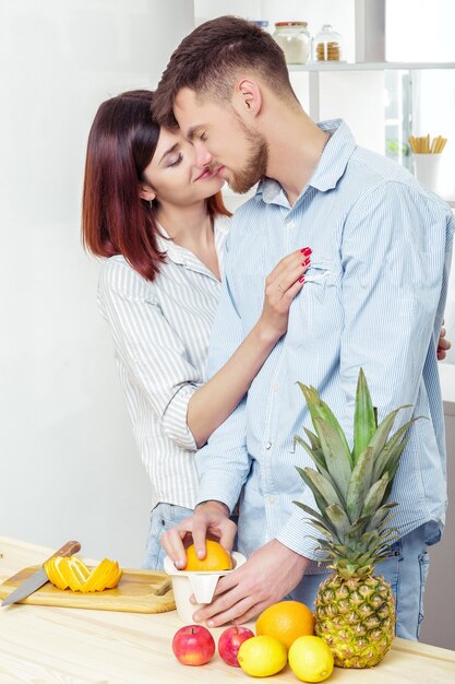 Coppie felici nell'amore in cucina facendo un sano succo di arancia fresca. la coppia sta baciando