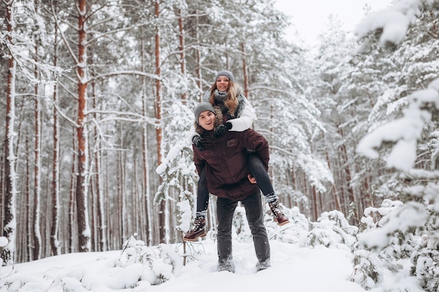 Coppie felici nell'amore in inverno in un bosco innevato giocando e sorridendo felicemente