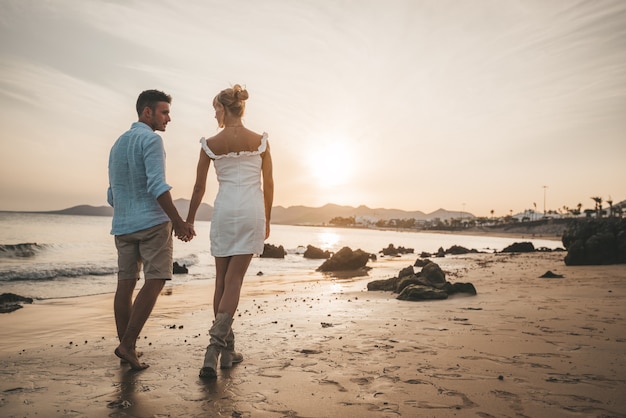 Coppie felici romantiche nell'amore che camminano sulla spiaggia al tramonto.