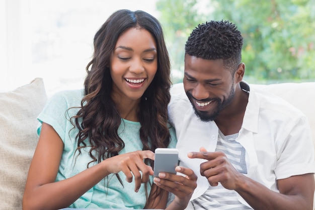 Coppie felici sullo strato facendo uso del telefono