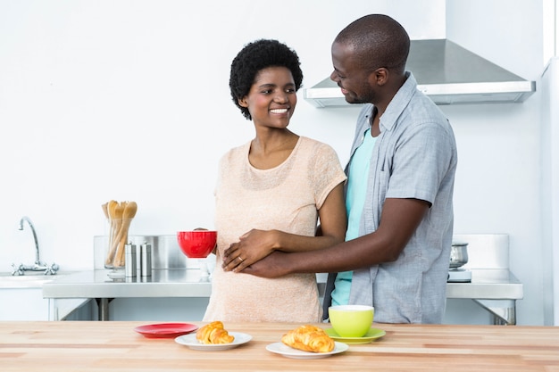 Coppie incinte sorridenti che mangiano prima colazione in cucina a casa