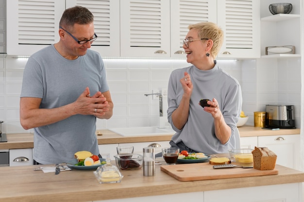 Coppie maggiori sorridenti che cucinano cibo sano con verdure fresche sane sulla cucina