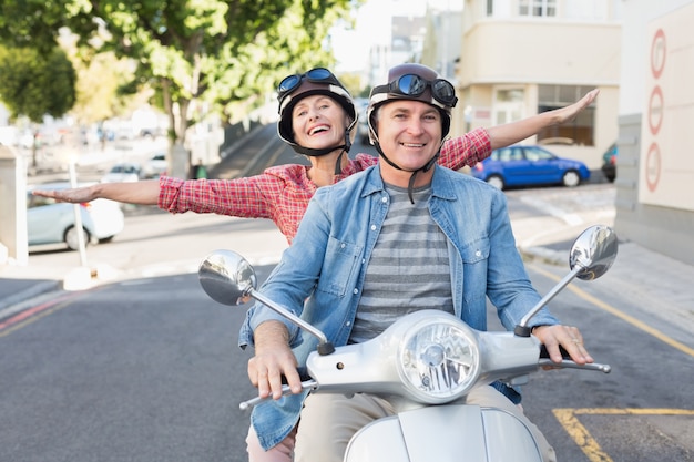 Coppie mature felici che guidano un motorino nella città