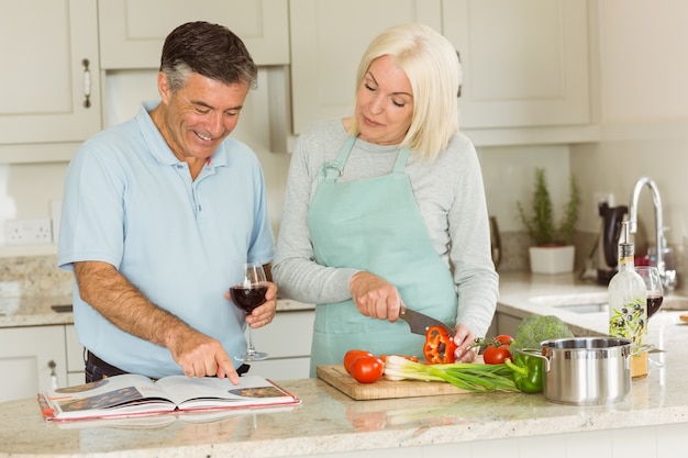 Coppie mature felici che mangiano vino rosso mentre facendo cena