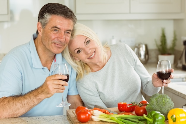 Coppie mature felici che mangiano vino rosso mentre facendo cena