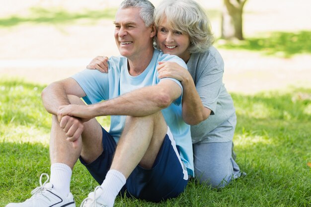 Coppie mature sorridenti che si siedono sull&#39;erba al parco